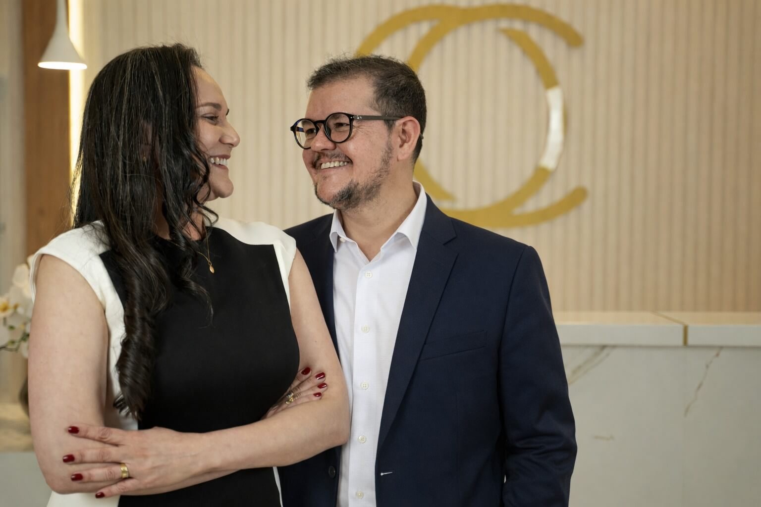 Dr Caio e Dra Larissa Fundadores da Clínica Odontológica Freitas Odontologia. Dentista em Campinas Especialistas em Implante Dentário e Faceta de Porcelana (lentes de contato dental em porcelana). Atrás, uma parede da clínica com a logotipo da Freitas Odontologia.