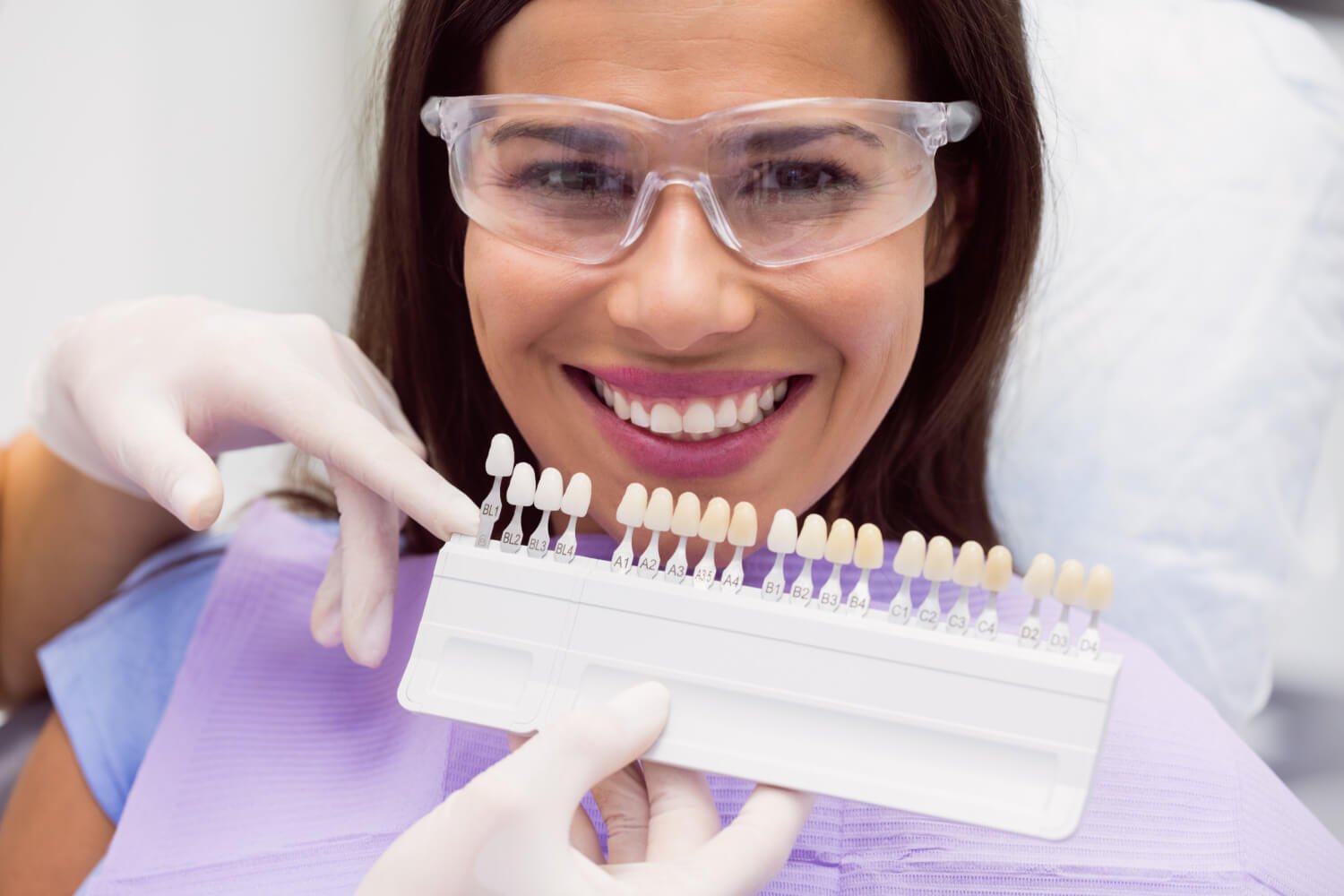 Paciente sorrindo feliz na cadeira odontológica enquanto o especialista avalia a cor ideal para facetas de porcelana em Campinas.
