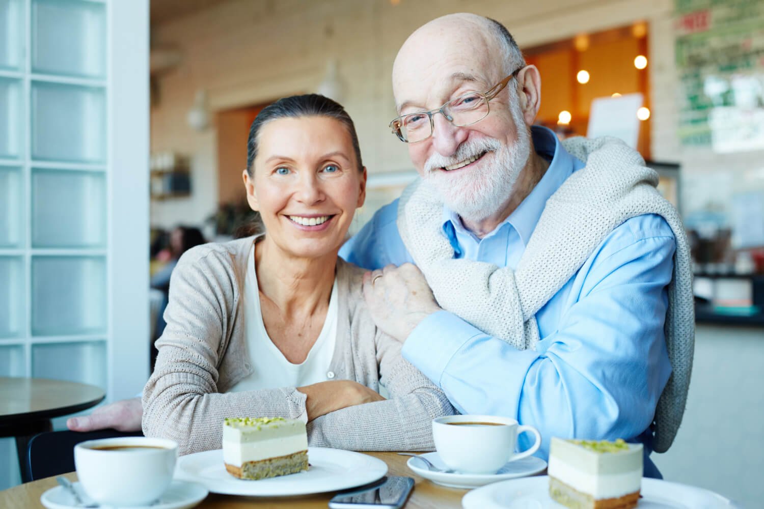 Casal idoso sorrindo feliz em uma cafeteria, desfrutando da segurança ao sorrir e comer com a prótese protocolo e carga imediata em Campinas.