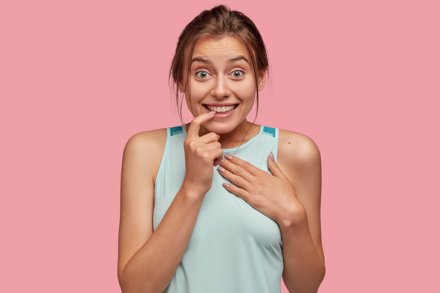 Mulher jovem com expressão de surpresa preocupada, apontando para os dentes após fraturar lente de contato dental em Campinas.