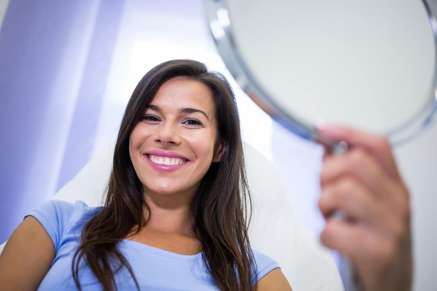 Mulher sorridente na cadeira odontológica olhando espelho e admirando o resultado do planejamento digital de lentes de contato dental em Campinas.