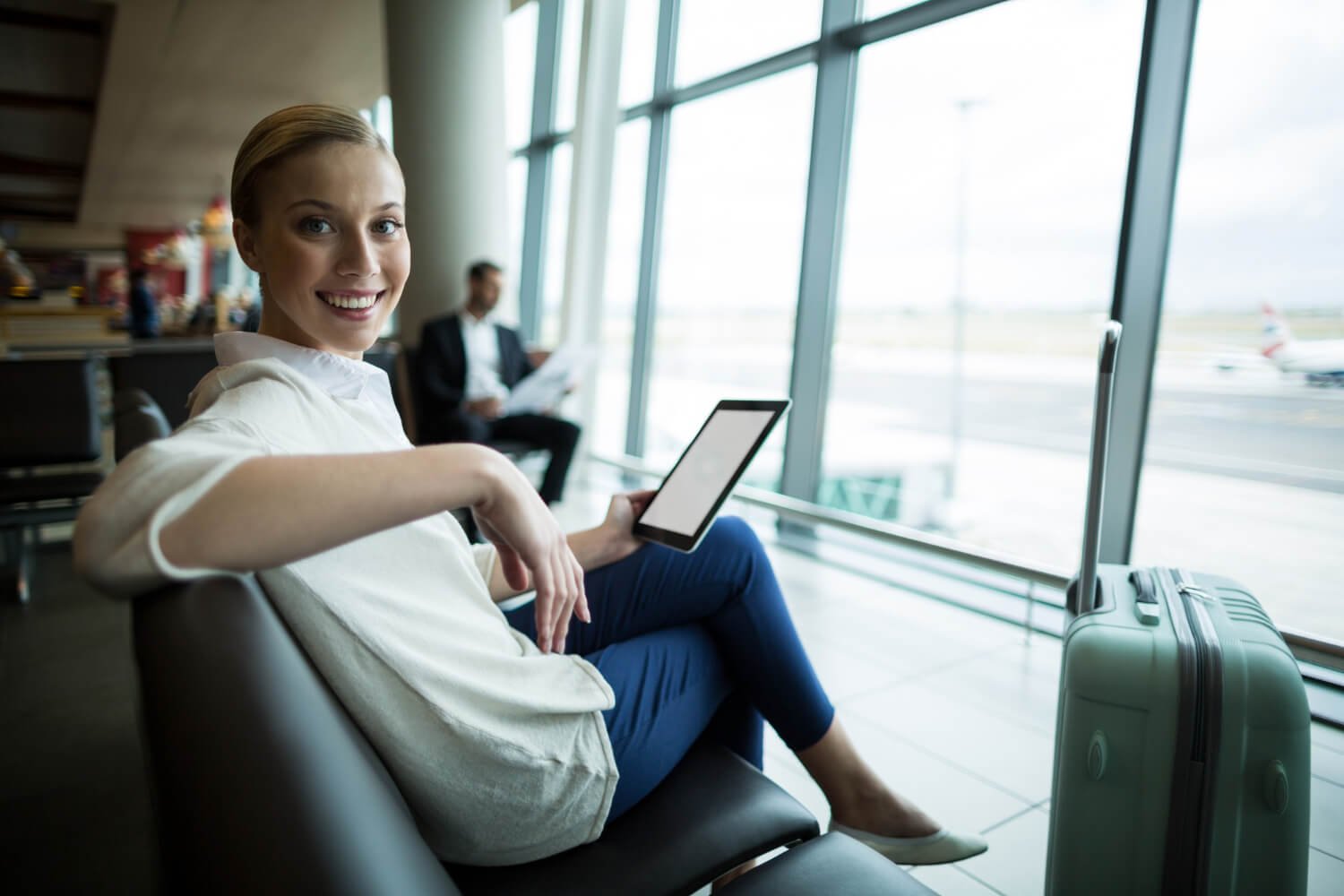 Mulher sorridente no aeroporto segurando tablet e mala, representando a praticidade de usar alinhadores invisíveis em Campinas.