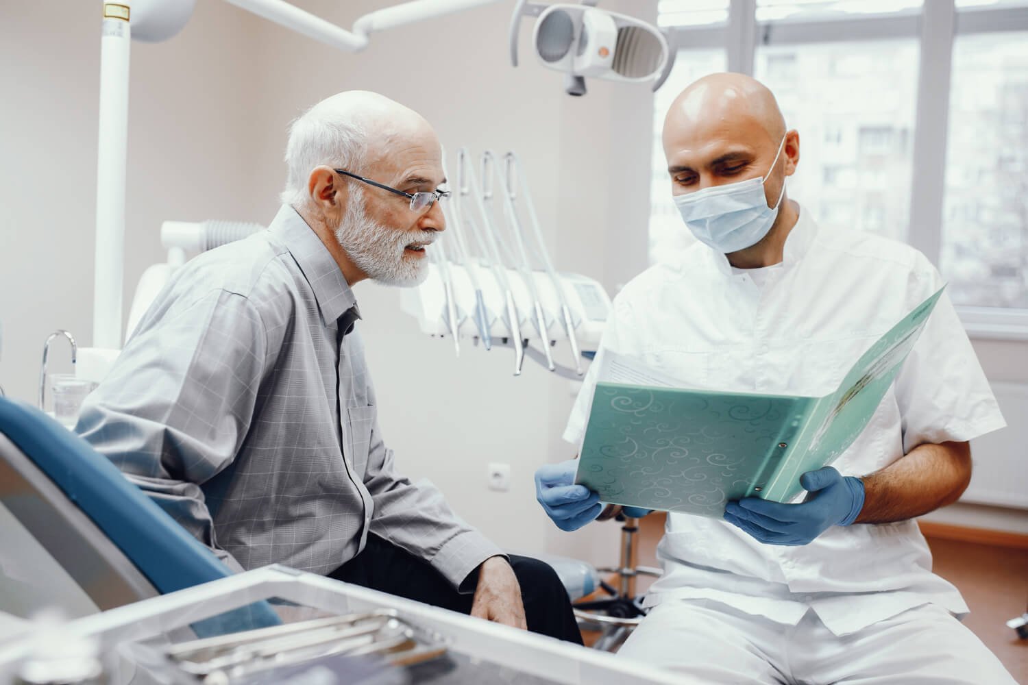 Homem idoso no consultório odontológico em consulta com o dentista sobre o tempo e etapas da cirurgia de implante dentário em Campinas.