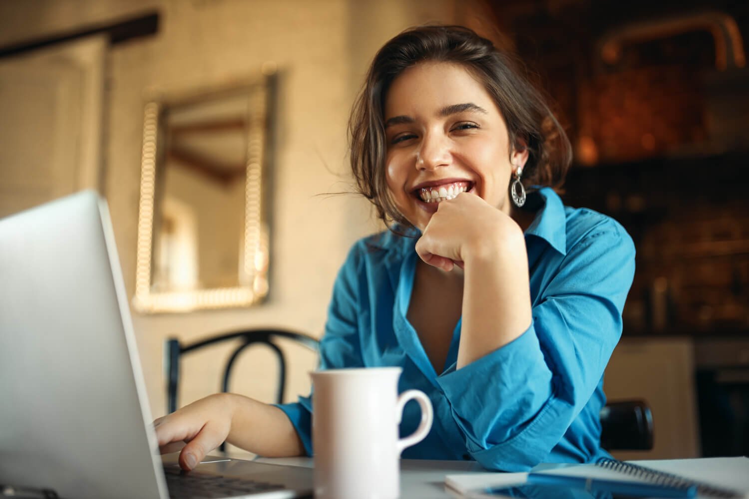 Mulher jovem sorrindo em frente ao laptop, exibindo dentes naturais que mostram como escolher a cor das facetas de porcelana em Campinas.
