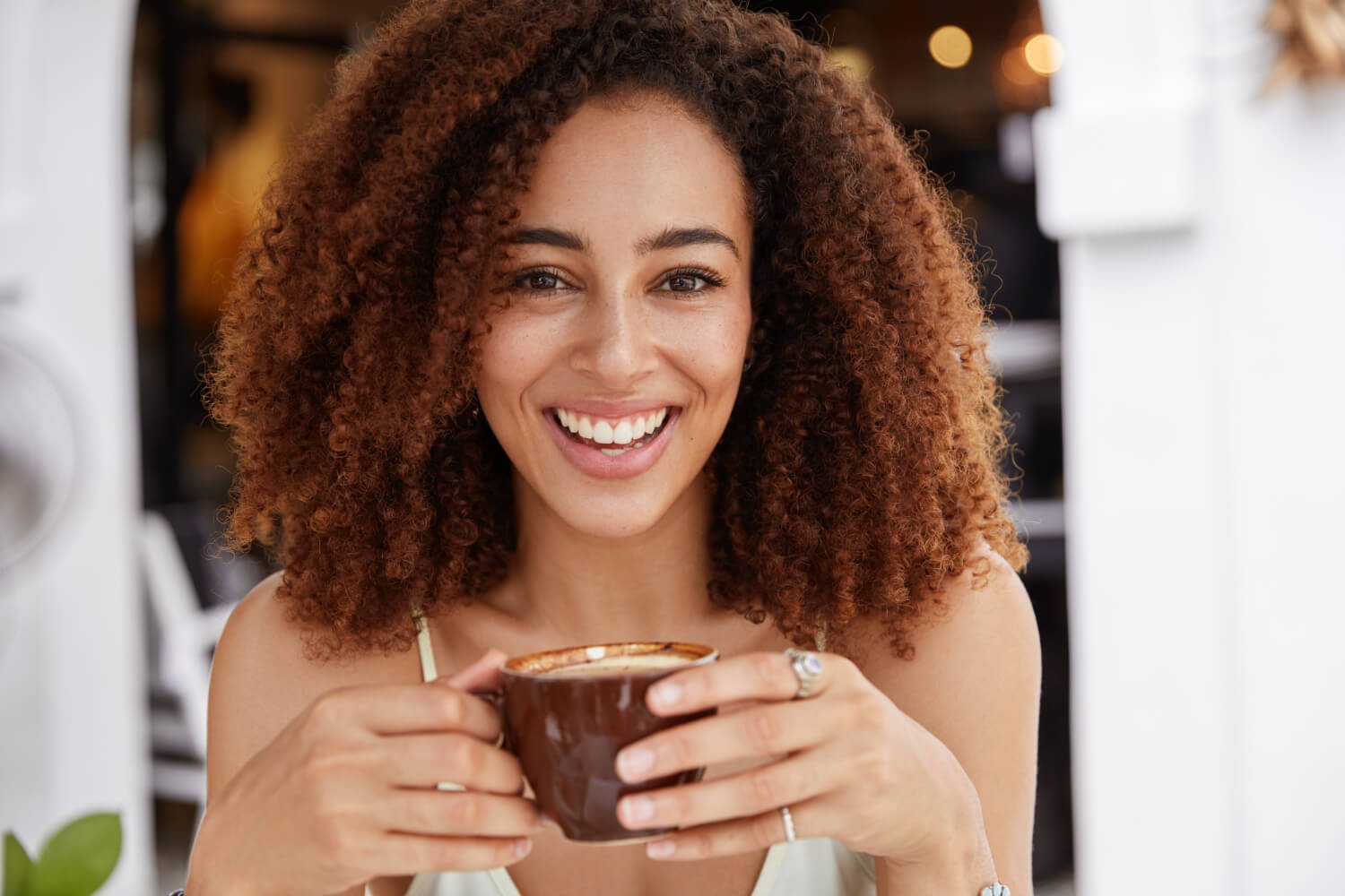 Mulher de cabelo cacheado sorrindo com xícara de café sobre facetas de porcelana mancham na Freitas Odontologia em Campinas SP.